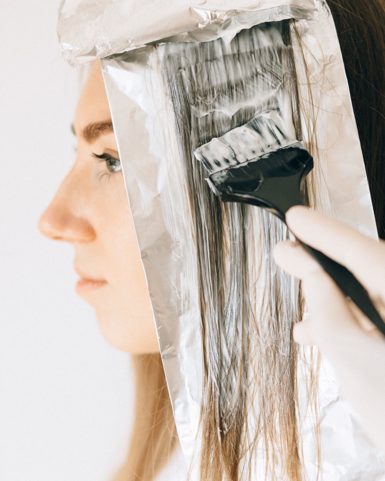 Friseurin trägt Haarfarbe mit einem Pinsel auf Strähnen in Folie auf